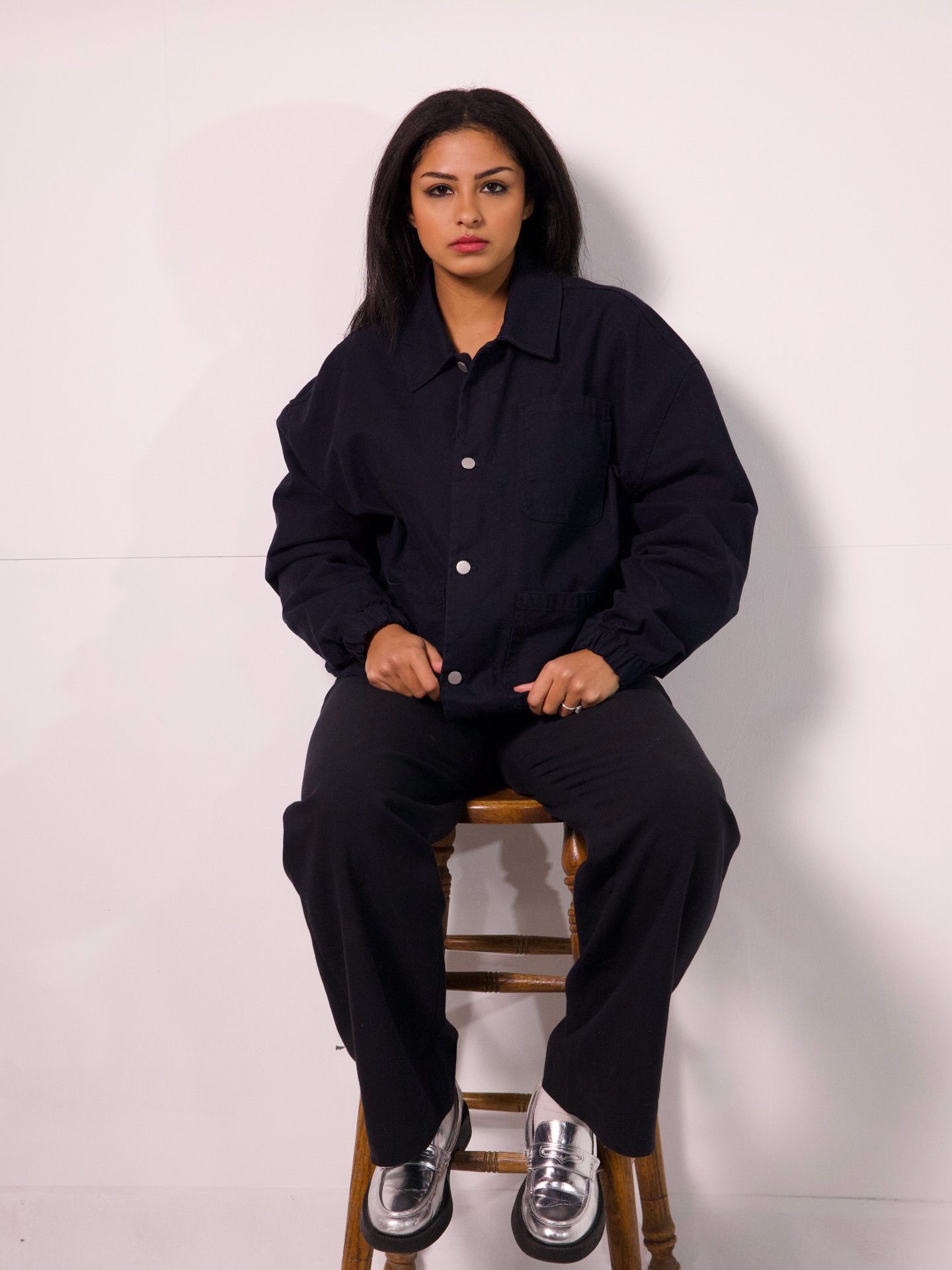 Noelani seated on a wooden stool in a black jacket and trousers